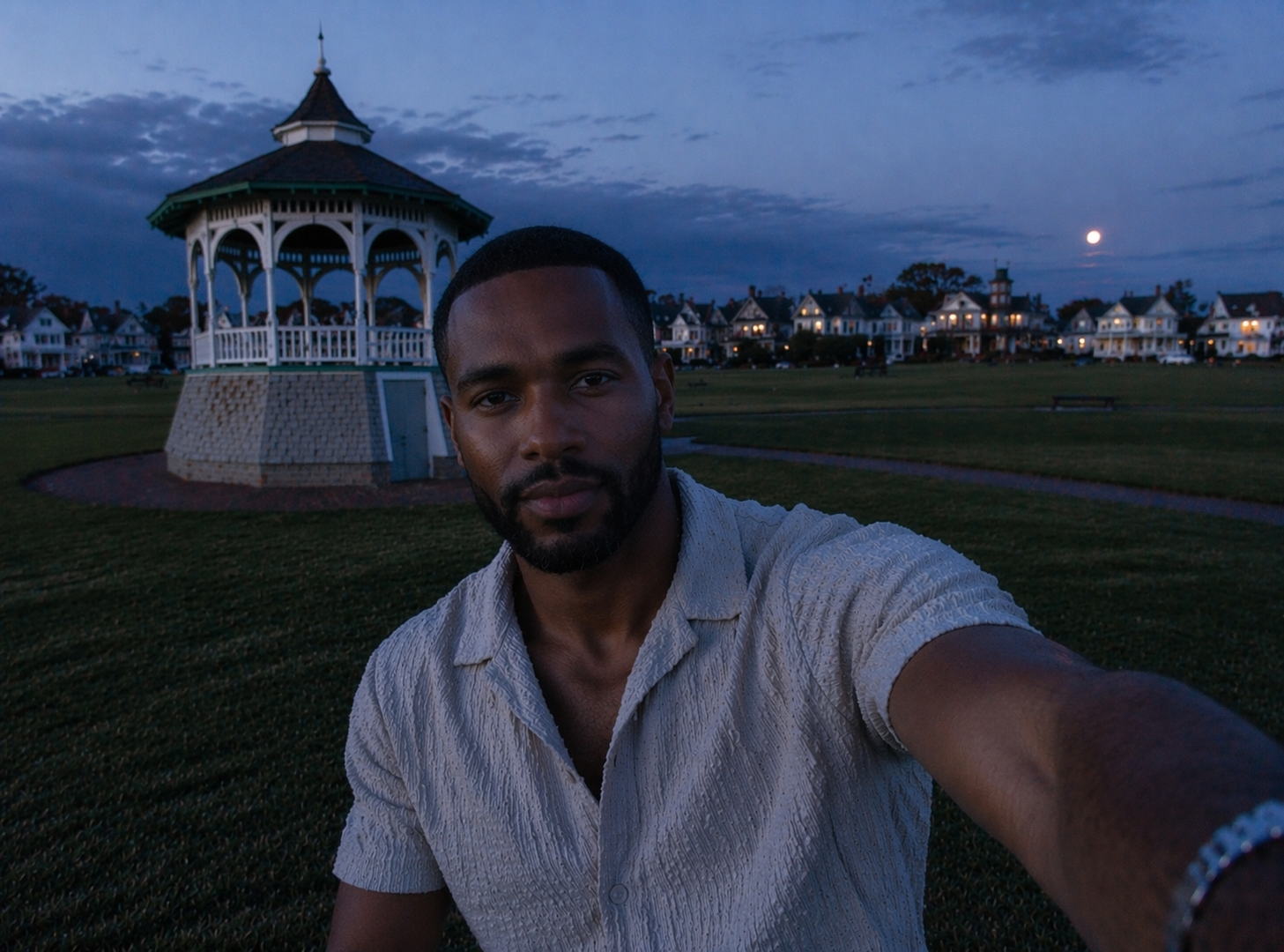 Malik Carter, founder of Black Vineyard Events, outdoors at dusk on Martha's Vineyard near a white gazebo with Victorian houses and warm window light in the distance.